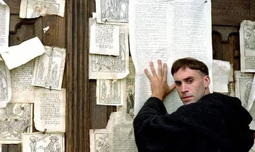 Cena do filme "Lutero", em que o personagem vive o tão citado episódio, no qual ele prega uma folha com as 95 teses da Reforma Protestante na porta de uma igreja. (Imagem: Youtube / Reprodução)