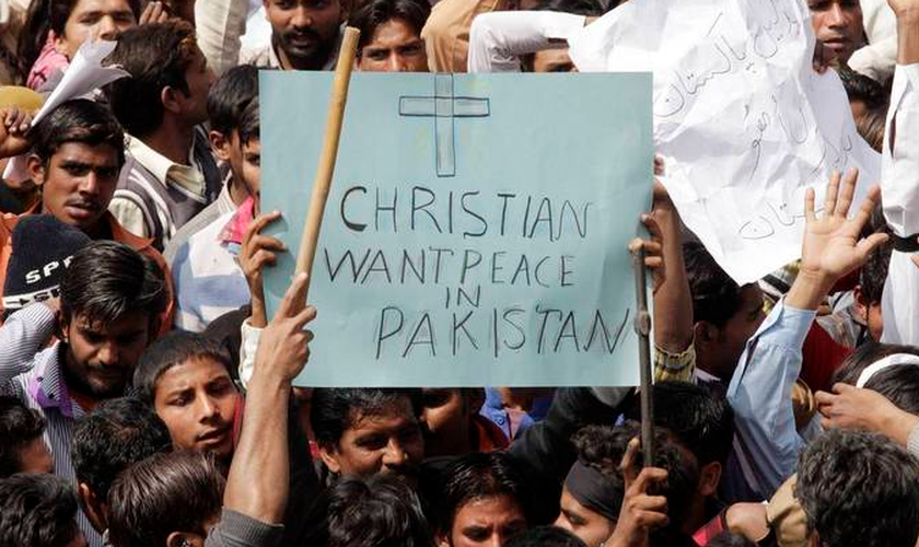 Homem segura em meio à multidão, cartaz que diz "Cristãos querem paz no Paquistão"