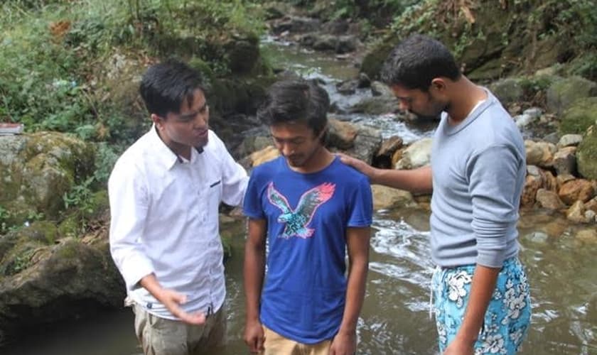 Pastor Lazrus e outro membro de sua equipe oram com jovem, antes de seu batismo, realizado em uma pequena cachoeira da região. (Foto: Levitas Nepal)