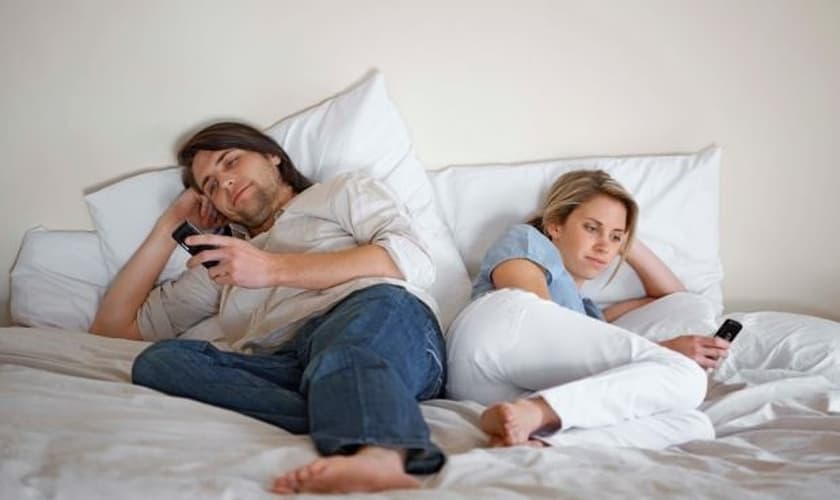 Casal usando celulares na cama. (Foto: Getty)