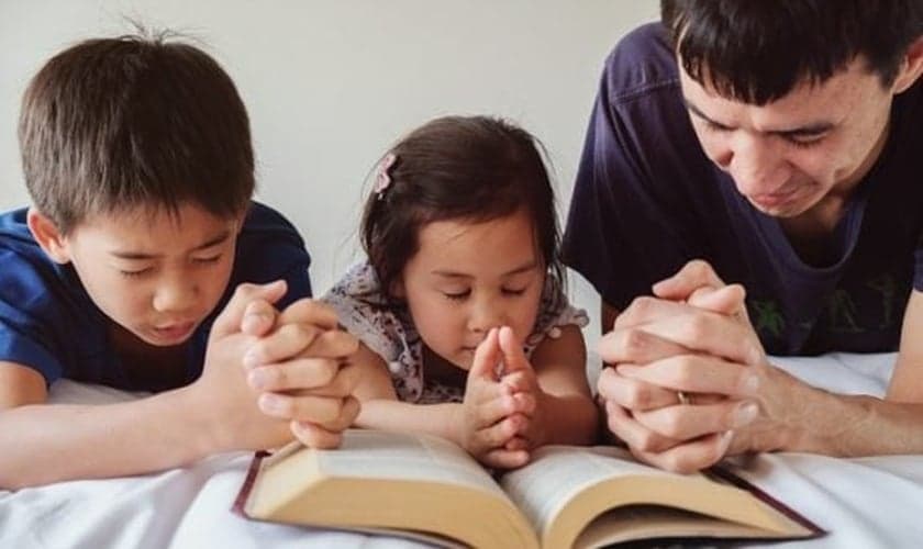 Pai lê a Bíblia com filhos. (Foto: Getty)