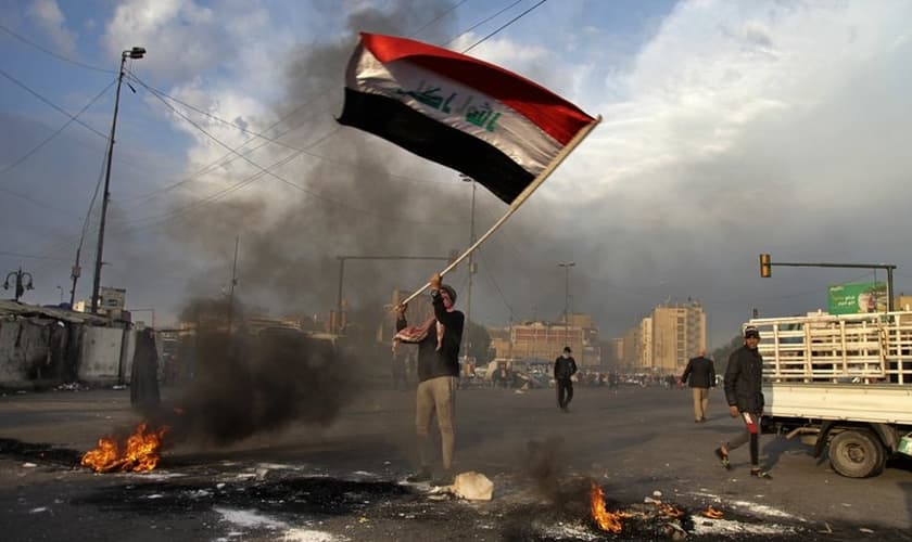 Manifestante acena a bandeira do Iraque enquanto fogo é ateado nas ruas próximas à Praça Tahrir, no Egito. (Foto: AP/Khalid Mohammed)