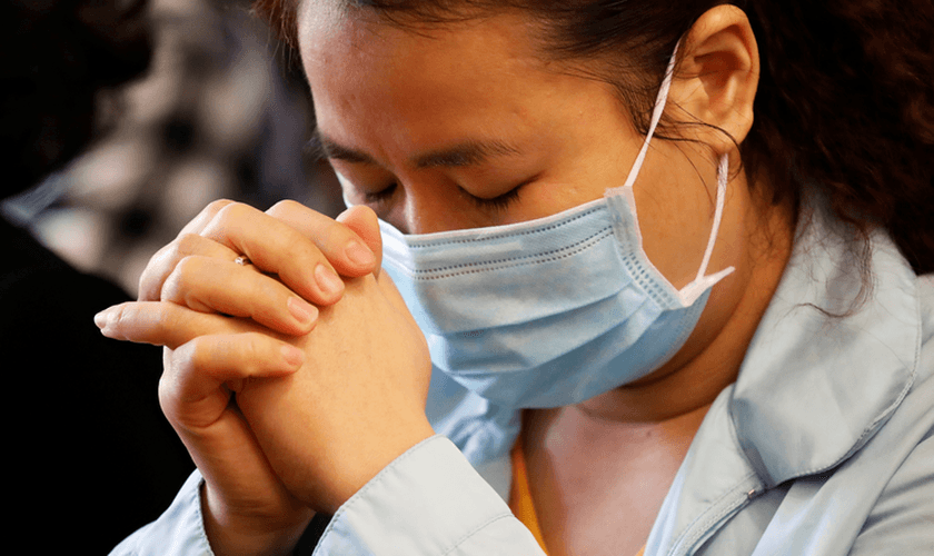 Uma mulher usa máscara enquanto ora em meio ao surto de coronavírus. (Foto do CNS / Kham, Reuters)