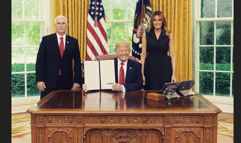 Donald Trump exibe a assinatura da ordem, entre a primeira-dama Melania e o vice Mike Pence. (Foto: Reprodução/Twitter)