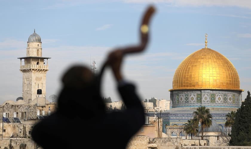 Homem toca shofar com o Monte do Templo ao fundo, em Jerusalém. (Foto: Reuters/Ammar Awad)