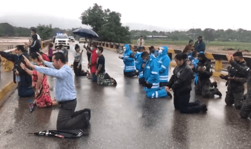 Policiais oram com cristãos em uma ponte sobre o rio Ulúa. (Foto: Policía Nacional de Honduras)