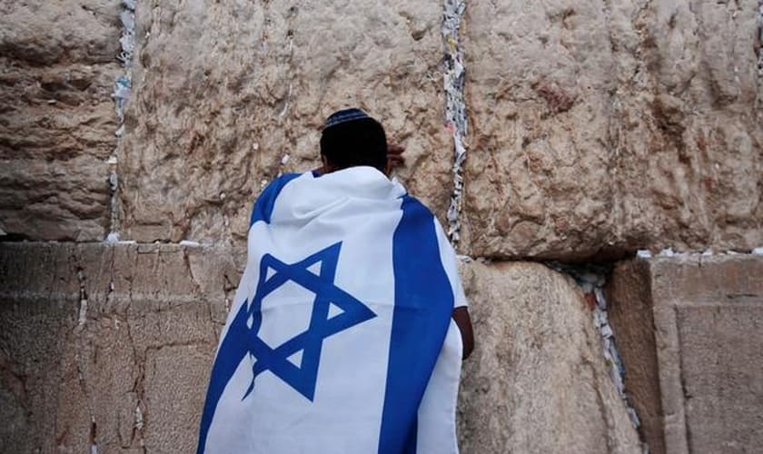 Jovem durante oração no Muro das Lamentações, coberto com a bandeira de Israel. (Foto: Reuters/Darren Whiteside)