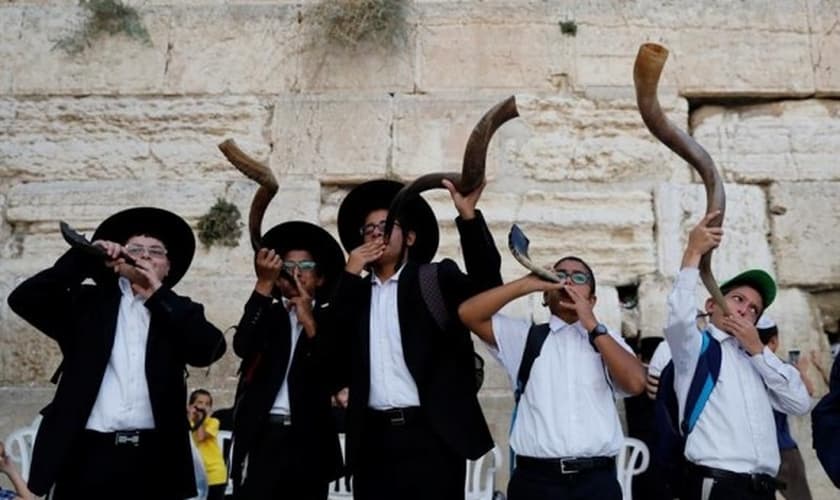 Judeus ultraortodoxos tocam o shofar enquanto os fiéis oram no Muro das Lamentações. (Foto: Reprodução / El País)